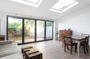 Ein geräumiges Zimmer mit einem großen Schiebeglasfenster, das in einen Garten führt, einem Esstisch mit Stühlen und einer Couch.