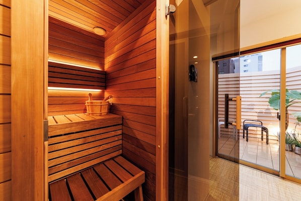 Un sauna en bois, avec des bancs et un seau, une porte en verre donnant sur l’extérieur et une vue sur le patio.