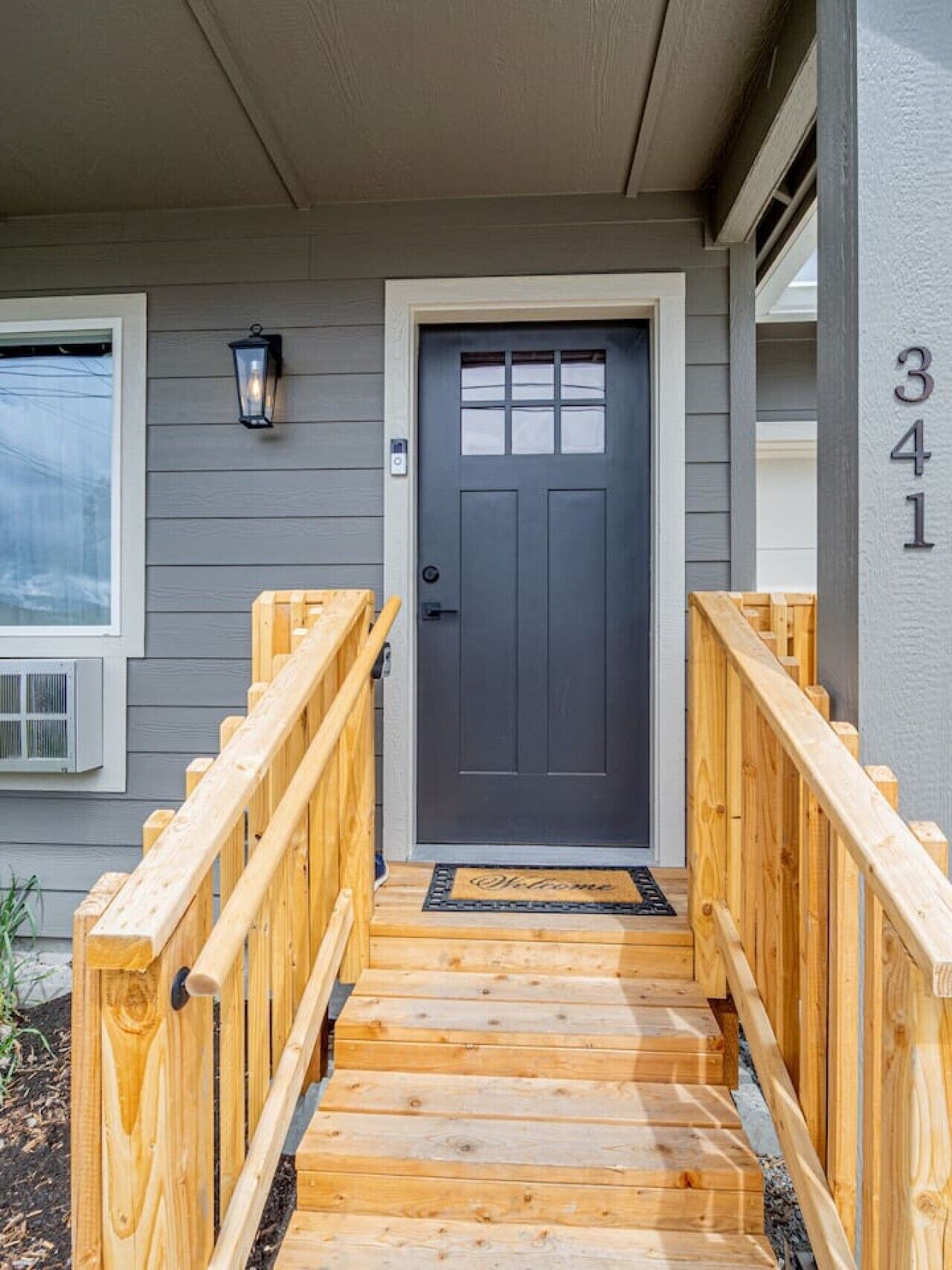 Un escalier en bois mène à une porte d’entrée de couleur sombre, sur laquelle est affiché le numéro « 341 ».