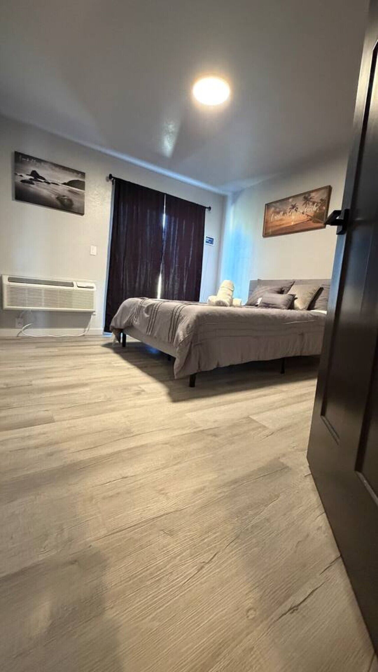 A bedroom with a bed, a window with curtains, and a wall-mounted air conditioner.