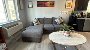 Un salon moderne avec un canapé d’angle, une petite table et un coin cuisine à l’arrière-plan.