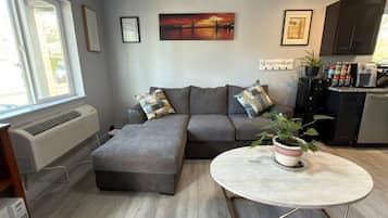 En moderne stue med en hjørnesofa, et lille bord og et køkkenområde i baggrunden.