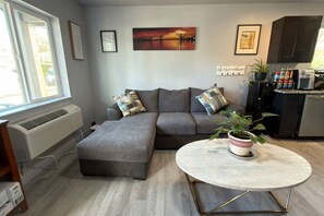 A modern living room with a sectional sofa, a small table, and a kitchen area in the background. - New Furnished 3+ bedroom house free WiFi & Park (Klamath Falls)