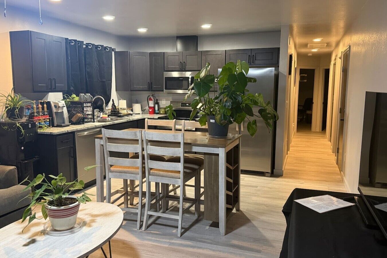 A modern kitchen with dark cabinets, a stainless steel refrigerator, and a dining area with a wooden table and chairs.