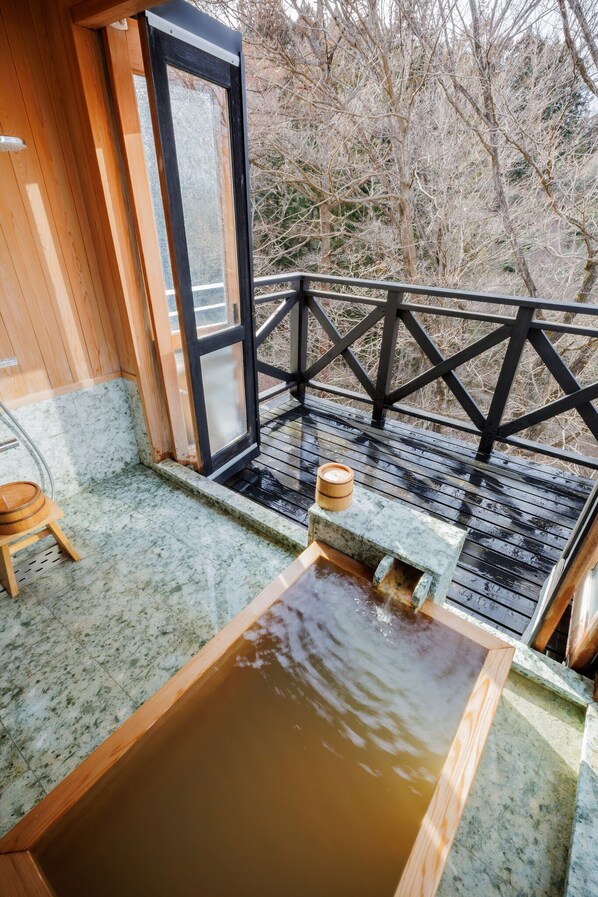 Un área de spa de madera con un jacuzzi, un taburete de madera y un banco de piedra.