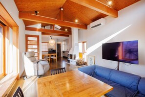 Un espacio habitable amplio con techo de madera, un televisor de pantalla plana grande, un sofá y una mesa de comedor.