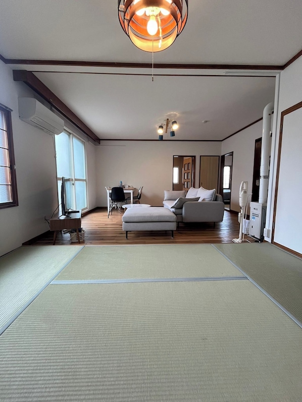 Ein Zimmer mit Tatami-Matten, einer Couch, einem Schreibtisch mit Stuhl und einer Deckenleuchte.