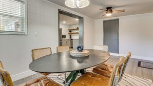 Zona pranzo con tavolo rotondo, sedie in pelle, lampadario e ventola a soffitto.