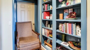 A room with a striped armchair, a bookshelf with books and decorative items, and a door with a light switch. - Gassville Group Getaway! Dog-Friendly Home + Yard (Gassville)