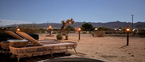 Une terrasse en bois avec un jacuzzi, des chaises longues et un paysage désertique avec des montagnes en arrière-plan.