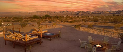 A desert landscape with a wooden deck, lounge chairs, and a fire pit.