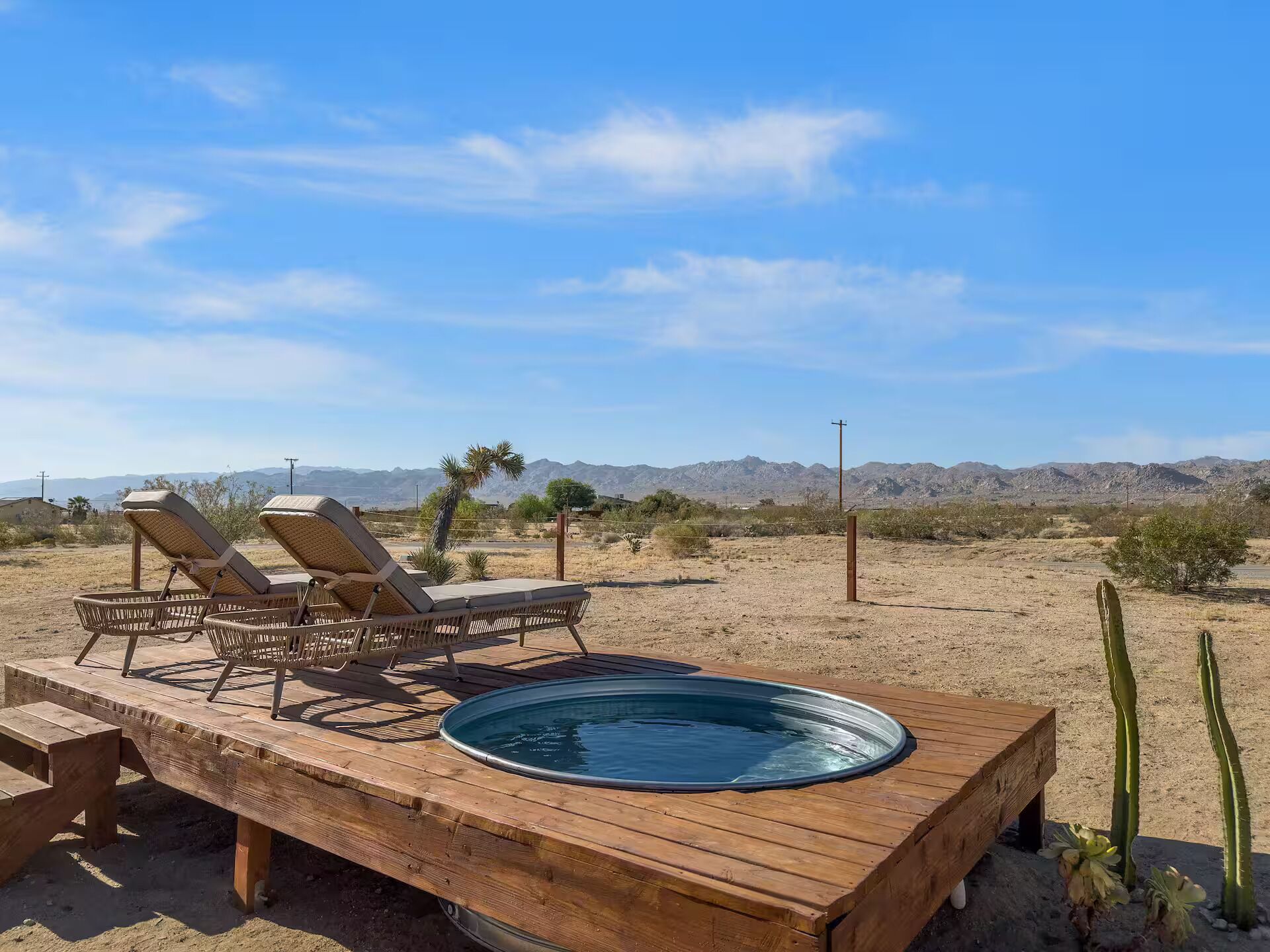 A wooden deck with lounge chairs and a hot tub in a desert landscape.