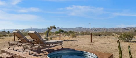 A wooden deck with lounge chairs and a hot tub in a desert landscape.