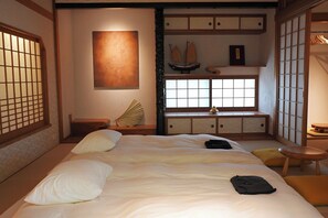 Ein traditionelles japanisches Schlafzimmer mit Tatami-Böden, einem niedrigen Plattformbett, einem Shoji-Bildschirm und einem kleinen Holztisch.