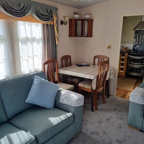 A living room with a sofa, dining table, chairs, and a kitchen area with an oven.