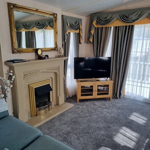 A living room with a fireplace, a television on a wooden stand, and a large mirror above the fireplace.