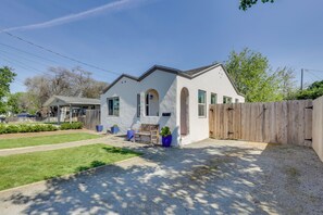 A single-story house with a white exterior, a wooden fence, and a small patio with a bench and potted plants.