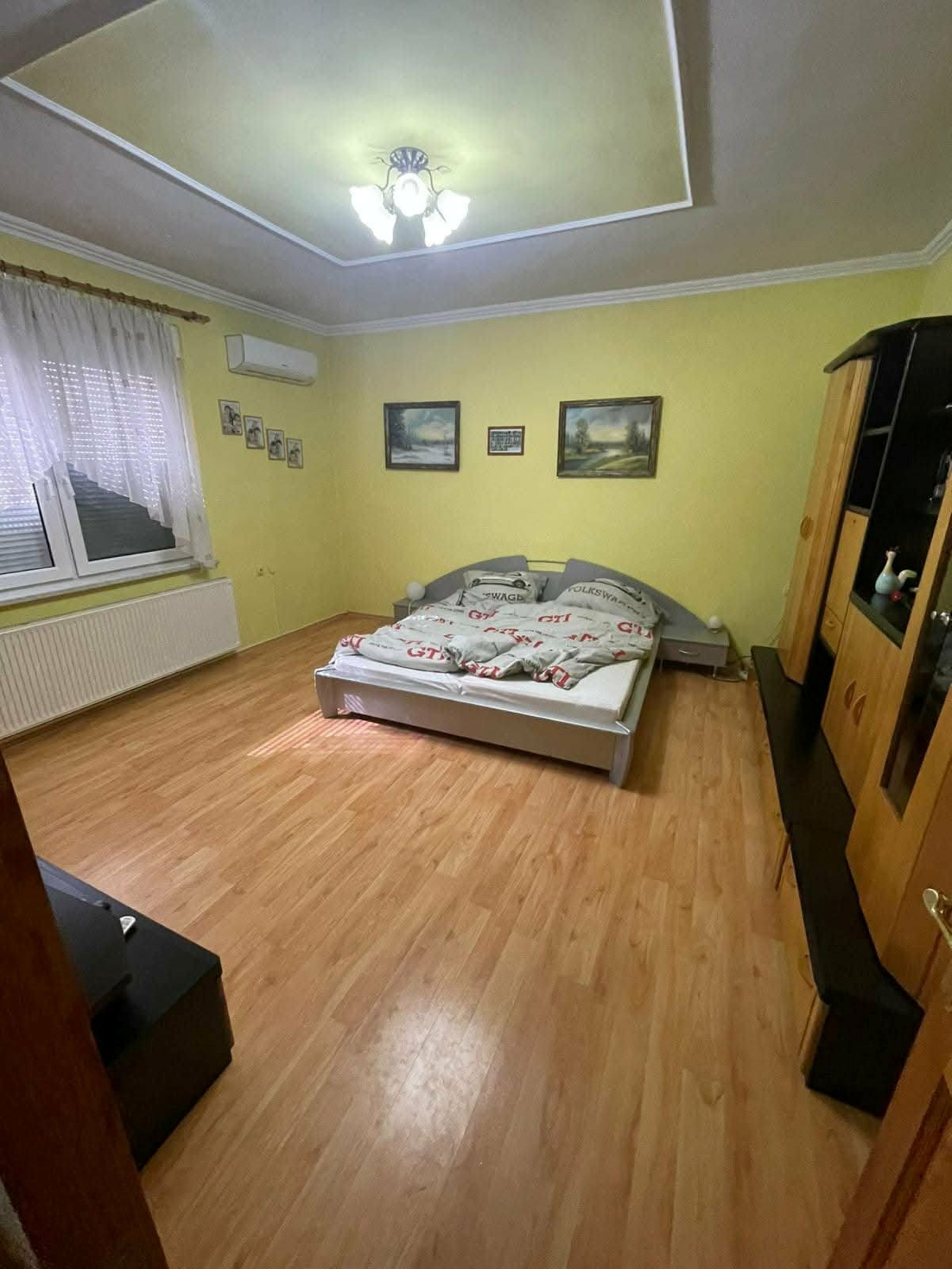 Une chambre à coucher avec un lit, un plancher en bois, un ventilateur de plafond et une fenêtre avec des rideaux.
