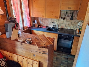 A kitchen with wooden cabinets, a sink, a stove, and various kitchen utensils.
