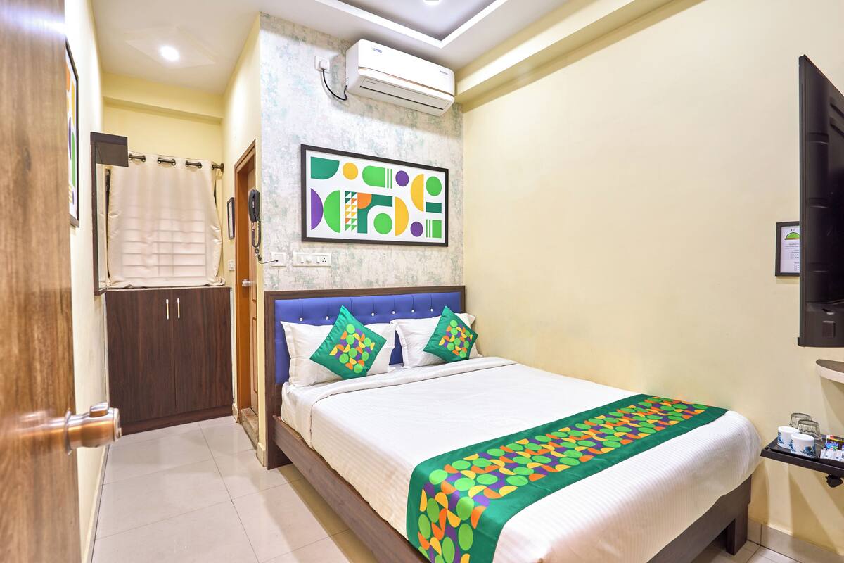 Habitación de hotel con una cama, aire acondicionado de pared, una obra de arte abstracta enmarco y una mesita con una taza y un control remoto.