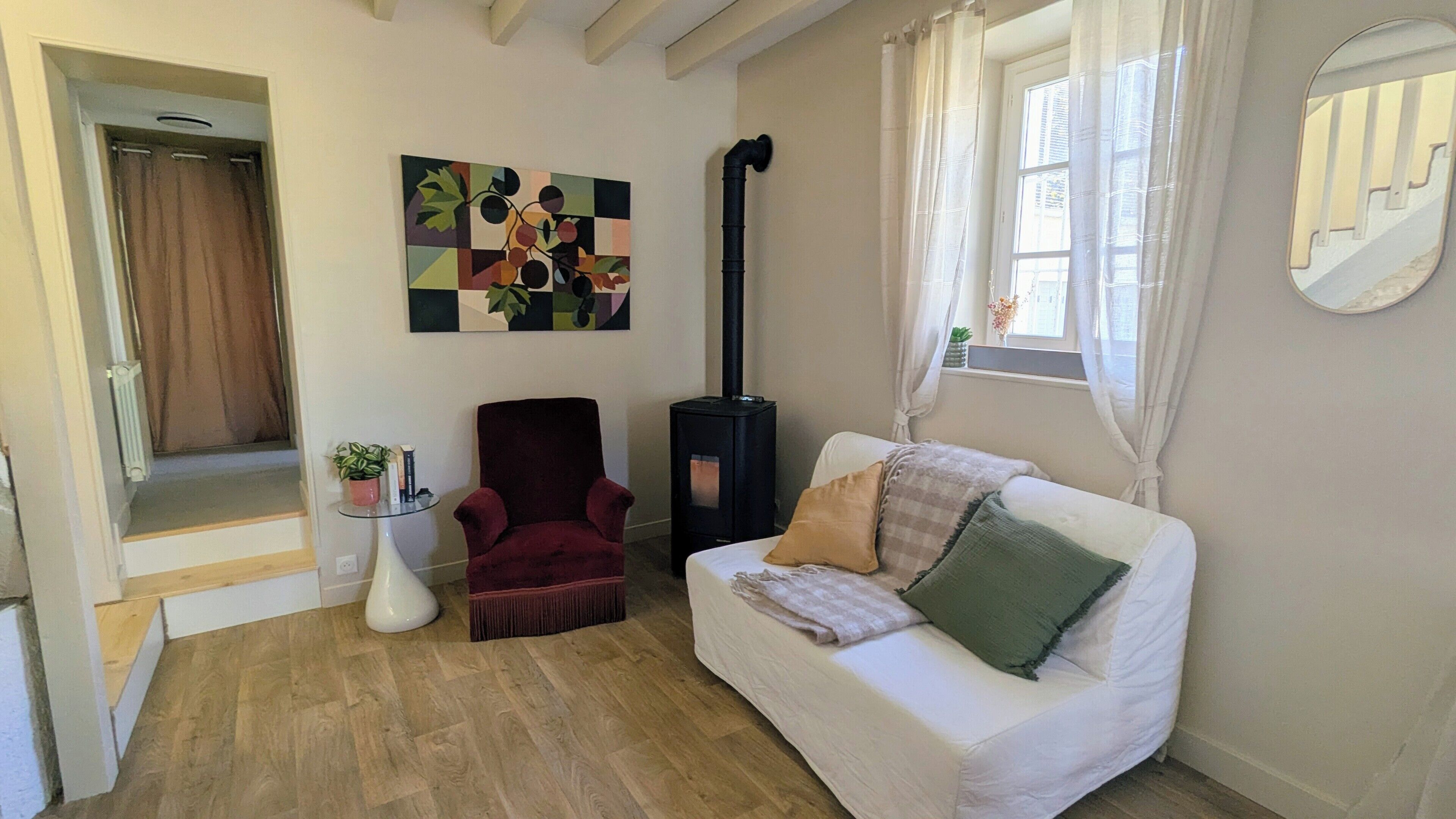 Uma sala de estar com um sofá branco, uma poltrona vermelha, um fogão a lenha preto e um quadro na parede.