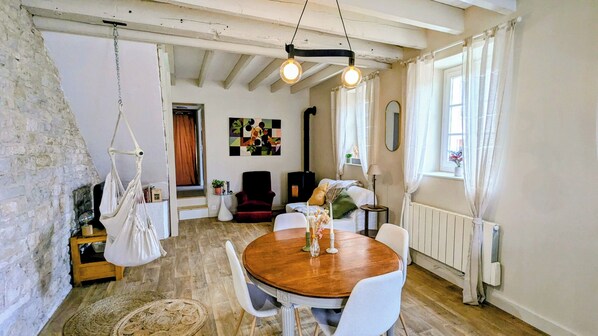 Une pièce chaleureuse avec une table à manger en bois, des chaises blanches, un fauteuil suspendu, un fauteuil rouge et une cheminée.