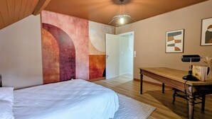 Ein Schlafzimmer mit einem Bett, einem Schreibtisch, einem Stuhl und einer Tür zu einem anderen Raum.