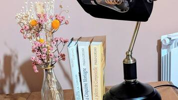 Een bureau met een zwarte bureaulamp, een glazen vaas met gedroogde bloemen en een stapel boeken.