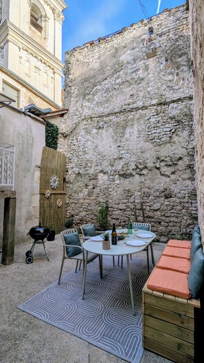 Une terrasse avec une table ronde, des chaises et un banc rembourré.