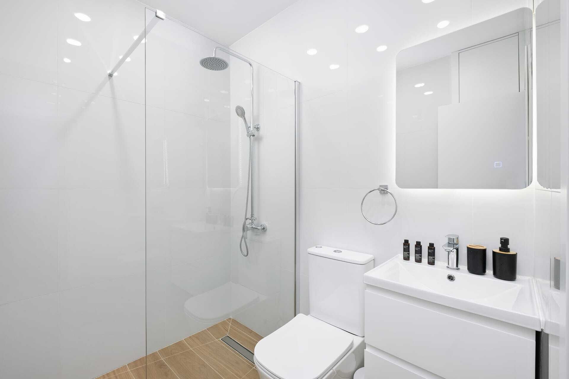 A modern bathroom with a glass-enclosed shower, a white toilet, and a vanity with toiletries.