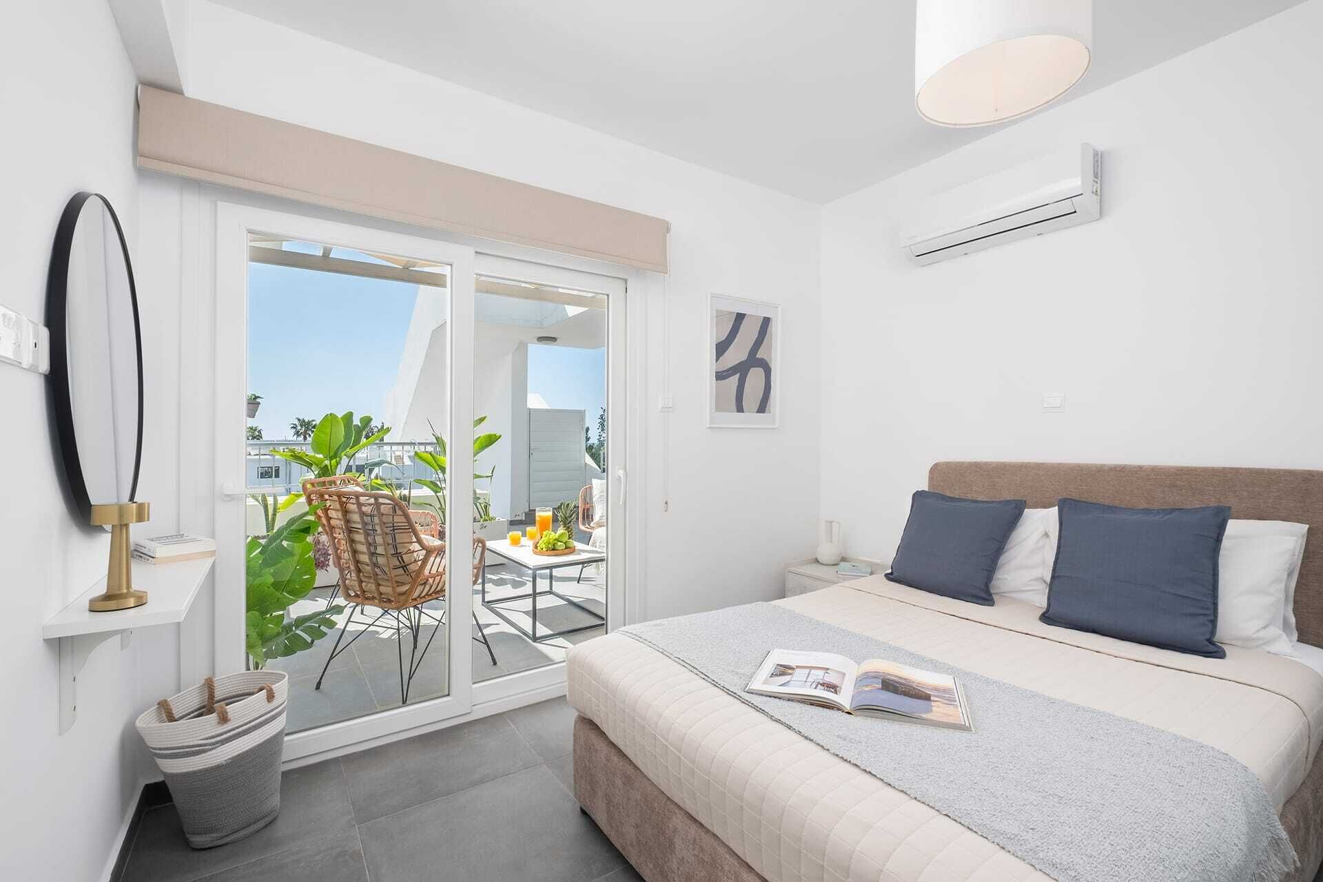 A bedroom with a bed, a bedside table, a window, and a view of the outdoors.