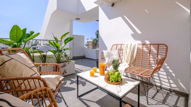 Terraza en la azotea con mobiliario de mimbre, una mesa con fruta y bebidas, y plantas en macetas.