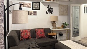 Una sala de estar con sofá, decoración en la pared, una guitarra y una lámpara.
