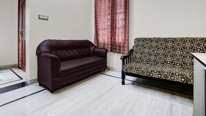 A room with a dark brown sofa, a patterned armchair, a red patterned curtain, and a light-colored tiled floor. - Premiumcoastal Inn 3 (Kakinada)