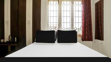 A bedroom with a bed, two black headboards, a window with metal bars, and a wardrobe.