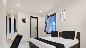 A bedroom with a bed, a chair, a door, a window with curtains, and a framed picture on the wall. - Premiumcoastal Inn 3 (Kakinada)
