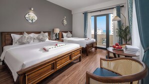 A hotel room with two beds, a balcony with a view, a small table with books and fruit, and a chair. - KLY Hotel & Retreat (Ho Chi Minh City)