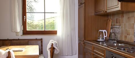 A kitchen with wooden cabinets, a stove, and a window with curtains.