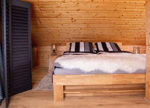 Une chambre à coucher aux murs lambrissés, avec un lit, des oreillers, une table de chevet et une lampe fixée au mur.