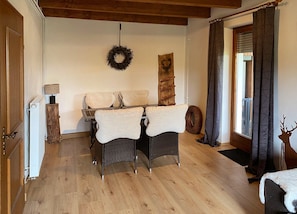 Une pièce avec un plancher en bois, une table à manger avec des chaises, une couronne décorative accrochée au mur, une échelle en bois et une fenêtre avec des rideaux.