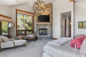 A spacious living room with a stone fireplace, a large TV mounted above it, and a cozy seating area with a sofa and armchairs. - Mountain Retreat • Hot Tub | Near Keystone Resort | Keystone Alpine Haven (Keystone)