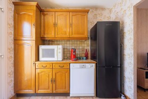 A compact kitchen with wooden cabinets, a white microwave, a black refrigerator, and a dishwasher. - La Brise de Valras – Air-Conditioned House (Valras-Plage)