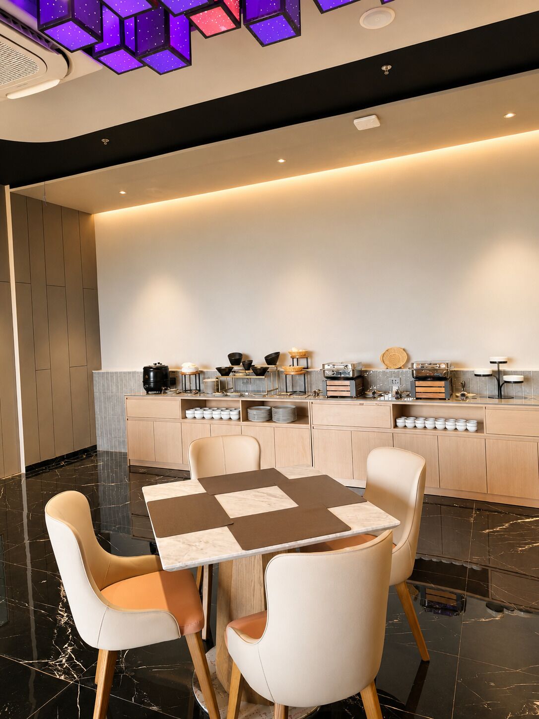 A modern kitchen with a marble countertop, a dining table with chairs, and a ceiling with geometric light fixtures.