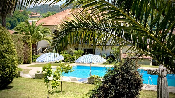 A pool area with two umbrellas, palm trees, and a building with a red roof. - Quinta Maria - 120 m² haven of peace with private swimming pool (Braga)