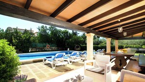 Área de piscina externa com espreguiçadeiras, mesa e estrutura de pérgola.