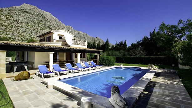 Piscina com espreguiçadeiras, um caminho de pedras e montanhas ao fundo.