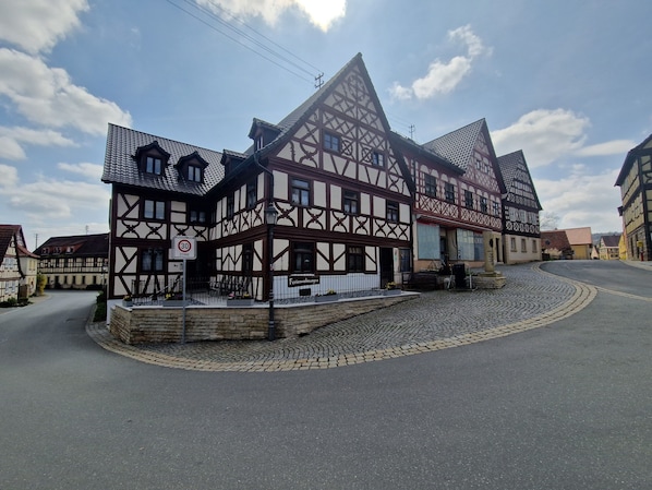 Un edificio tradicional de entramado de madera con una calle adoquinada, una señal de límite de velocidad de 30 km/h y un cartel que indica 'Ferienwohnungen'.