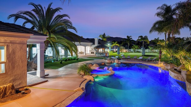 Una piscina con hidromasaje, palmeras y un patio bien iluminado.