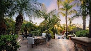 A patio area with a stone fire pit, outdoor seating, and lush greenery. - Sleeps 17 | Resort-Style Pool + Cabanas | Exclusive Poway Stay | Sunset Estate (Poway)