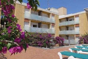 Un hotel de diverses plantes amb balcons, mobiliari exterior i plantes de buguivella.